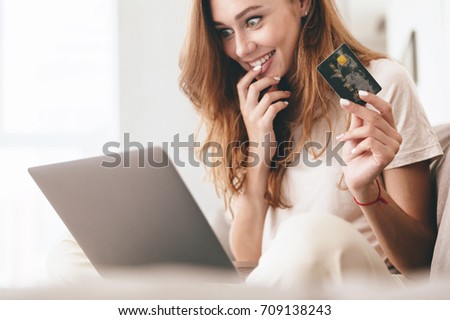 Cropped picture of young happy amazing pretty lady sitting on sofa indoors. Looking aside using laptop computer holding credit card.