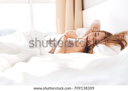 Image of young smiling pretty lady lies in bed indoors. Eyes closed.