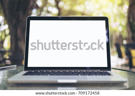 Mockup image of laptop with blank white screen on glass table at outdoor with green nature background