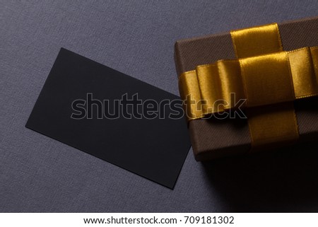Mockup black business card on dark gray background. Template for branding identity. Brown gift box with golden ribbon. Copy space. Flat lay style, view from above. Corporate gift concept.