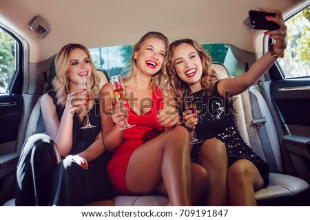 Women drinking champagne and make selfie in a limousine car. Royalty-Free Stock Photo #709191847