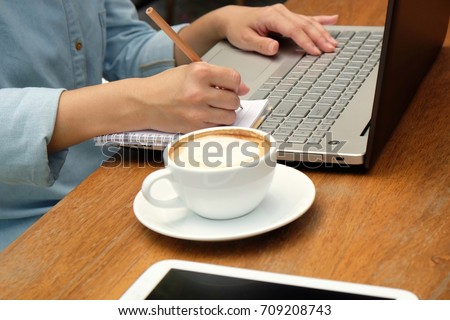 Hand of woman typing on laptop keyboard and writing on paper note, using computer with hand typing on keyboard