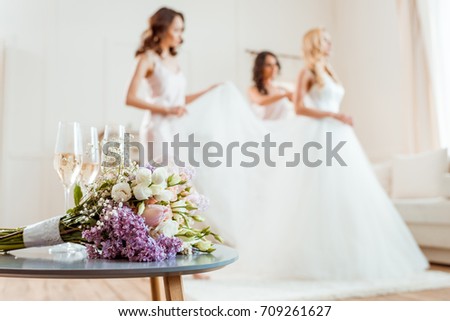 close-up view of champagne and wedding bouquet with bride and bridesmaids blurred on background