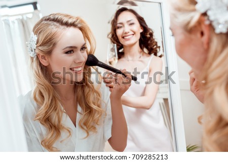 beautiful young bride getting makeup before wedding and looking at mirror
