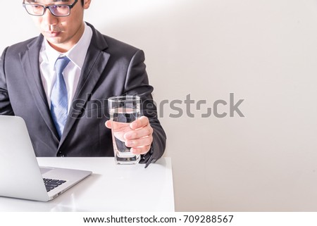 Asian business man working online and hold glass of water in the office, Man in suit and necktie type notebook on table, free space at right side on white background.