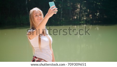 Young woman taking a selfie by a smartphone in a forest. Beautiful caucasian girl spending time in a moutain woods.