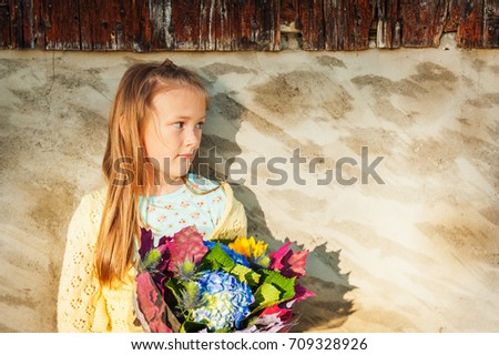 Outdoor portrait of a cute little girl holding beautiful bouquet of autumn flowers