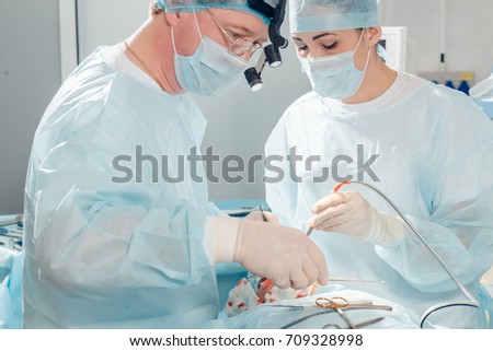 Surgeon performing cosmetic surgery on nose in hospital operating room. Surgeon in mask wearing surgical loupes during medical procedure