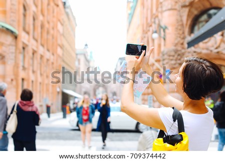 Back view attractive young female tourist taking picture of active life in the city with her smartphone camera, woman traveler photographing urban view with mobile phone, vacation holidays in summer