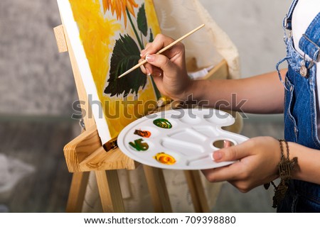 Artist's hand with brush and palette painting a picture Sunflower 