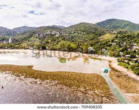 View from above of the tropical island, namely Koh Pha Ngan Island, with rocky beach of a small bay with the rain forest on a mountain during low tide with a blur view of mountain from afar