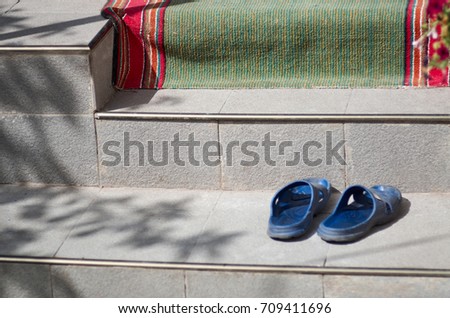 Blue sliders on steps of a house with open door, curtain lace and green-red footcloth/Sliders on the stairs