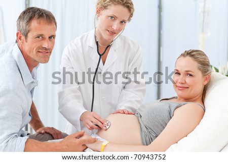 Pregnant woman with her husband and the nurse looking at the camera