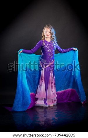 Portrait of a young girl with long hair in a purple costume oriental dancer with a blue shawl posing and dancing on a black background
