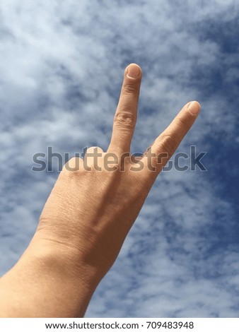 hand doing victory sign against blue sky