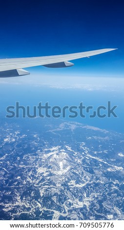 Aerial view from airplane window over Japan with airplane's wing,mountains covered snow and blue sky background.