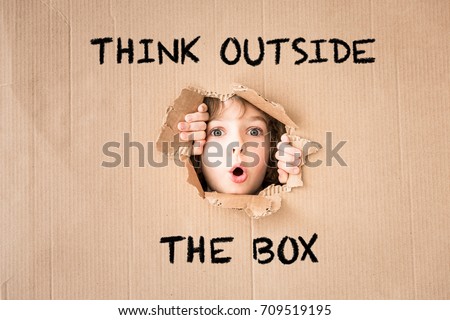 Portrait of funny child. Surprised child looking through hole of cardboard. "Think outside the box" concept