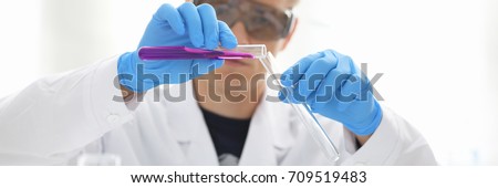 A male chemist holds test tube of glass in his hand overflows a liquid solution of potassium permanganate conducts an analysis reaction takes various versions of reagents using chemical manufacturing Royalty-Free Stock Photo #709519483