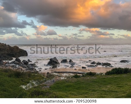 Stormy, moody, beach scene with rough foamy waves, jagged rocks and beautiful sunset