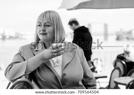 A woman of size plus a US or European look sitting in a restaurant drinks coffee in a good mood. A young girl with excess weight, stylishly dressed in the center of the city is waiting for a friend