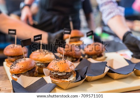 Chef making beef burgers outdoor on open kitchen international food festival event. Street food ready to serve on a food stall. Royalty-Free Stock Photo #709571101