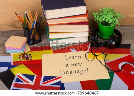Learning languages concept - paper with text "Learn a new language!", flags, books, headphones, pencils on wooden background Royalty-Free Stock Photo #709640467