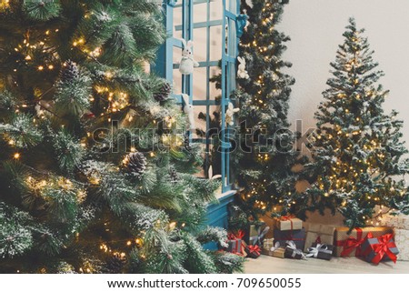 Decorated christmas trees background. Fluffy green pines in shiny garland and beautifully wrapped presents. Xmas and new year eve atmosphere, closeup, copy space