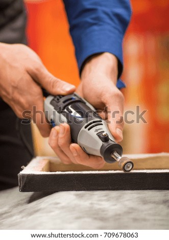Closeup of a hardworker man using a polisher in a wooden frame, on a gray table in a blurred background
