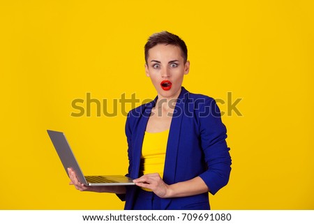 Shocked young business woman using laptop looking at you camera blown away in stupor standing on a yellow background. Human face expression, emotion, feeling, perception, body language, reaction