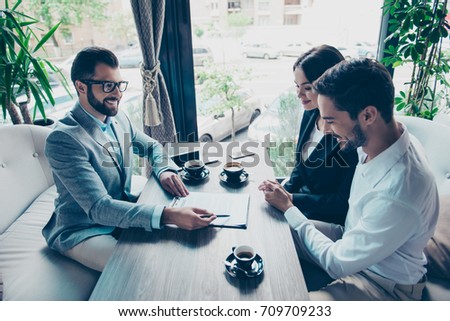 Business meeting at the restaurant. Happy couple is buying new house, young bearded attractive brunet lawyer in a formal wear is presenting contract to sign, they are having coffee