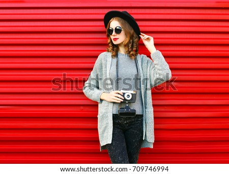 Fashion autumn portrait woman holds retro camera on a red background