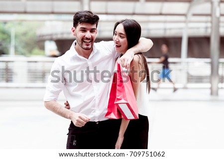 Happy couple talking after a hard day of huge sale shopping in asian country. Young handsome white male and beautiful asian female with red shopping bag looking very satisfy. Apply urban looks.