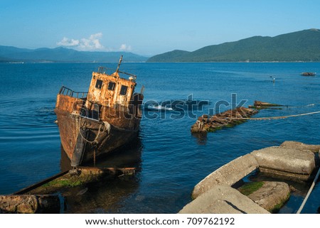 Small abandoned ship near the coast. Tilted rusty nautical longboat near the old pier. Royalty-Free Stock Photo #709762192
