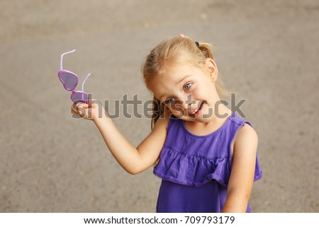 Cute little girl holding sunglasses. Portrait of a child.