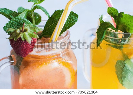 Close up fresh fruit cocktails in glass jar on light blue background. Orange and strawberry cold drink with mint and ice, refreshment in hot weather