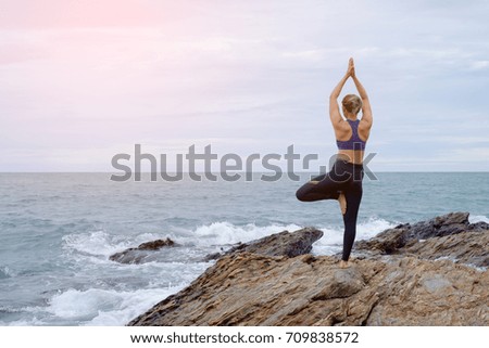 The woman practicing yoga on the beach at sunset.