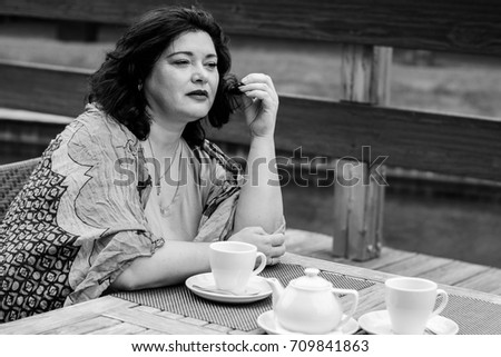 Mature woman in bright scarf, size plus american or European appearance sitting in a restaurant drinks coffee at autumn day. Lady with excess weight, stylishly dressed in cafe waiting for a friend