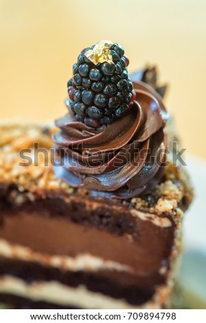 Closeup of fancy chocolate layer with blackberry topped by thin gold foil with focus on blackberry