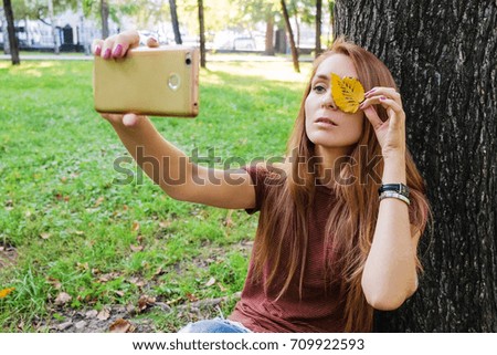 Hipster girl using her smartphone. Young successful woman sitting on social networks and read messages. Girl takes a picture of golden leaves on a mobile phone.