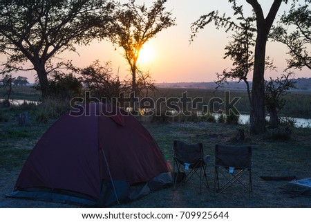 Camping tent, chairs and camping gear. Sunrise over Okavango River, Namibia Botswana border. Adventure traveling and outdoor activities in Africa. Toned image, vintage style.
