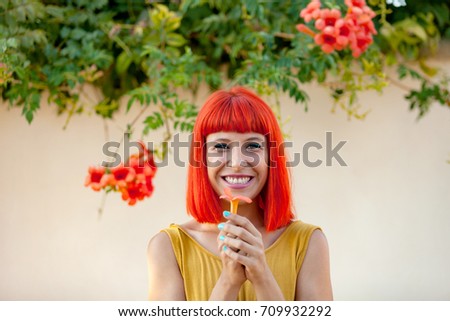 Happy woman with red hair and yellow dress near to a plant with beautiful flowers