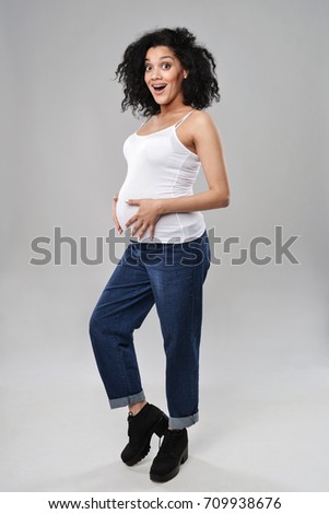 Pregnant woman standing in full length with expression of surprise, over grey background