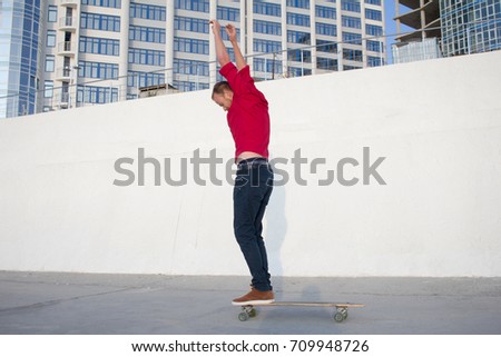 Young bearded man riding on skateboard, hipster with longboard in red 
shirt and blue jeans urban background   