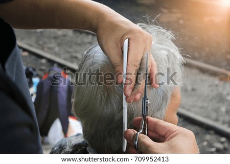 Master cuts hair and beard of men at outdoor barbershop, hairdresser makes hairstyle for an old man.