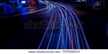Blue neon light trails from moving traffic at an intersection at night. Suitable for graphic or abstract design.