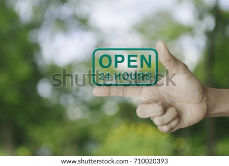 Open 24 hours icon on finger over blur green tree background