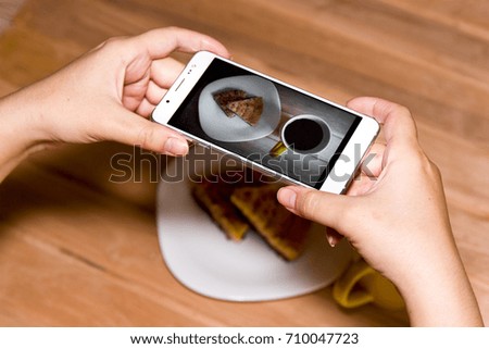 Using a mobile phone to photograph hot coffee and cookies on a wooden background with copy space. Photos of drinks and food for advertising or social media. Template.