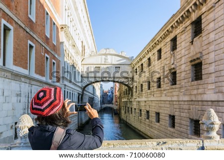 Female tourist taking picture of Ponte dei Sospiri bridge crossing canal from Ponte della Paglia, The famous travel destination of Venice near St. Mark's Square in Italy