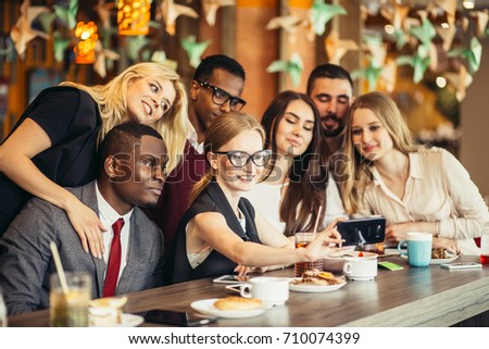 Group of happy smiling people taking a self-portrait in a cafe white having a break