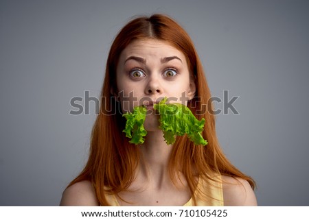 woman with big eyes eating lettuce on gray background portrait                               